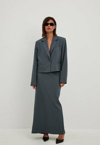 Conjunto de dos piezas que incluye un blazer corto gris con un solo botón y una falda larga a juego. Tejido suave, diseño minimalista.