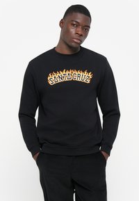 Zwarte sweatshirt met de tekst "SANTA CRUZ" in oranje vlammen erboven. Gemaakt van katoen, met ribgebreide manchetten en een ronde hals.