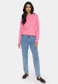 Spilgti rozā adīta džemperis ar garām piedurknēm, apvienots ar augsto vidukli gaiši zilām denima biksēm un brūniem loaferiem ar frinšu detaļām.