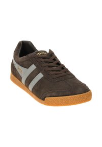 Zapatillas de ante marrón con rayas grises, suela de goma y punta redonda. Presentan cierre de cordones y detalle del logo dorado en la lengüeta.