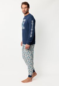 Camiseta de manga larga de color marino con diseño "ALOHA STITCH"; pantalones estampados con Stitch azul y flores de hibisco, con puños elásticos en color marino.