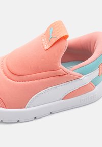 Chaussure de sport rose corail avec un design à enfiler, présentant un matériau textile lisse, des accents blancs et un détail de talon bleu clair.