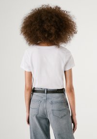 Hvit bomulls t-skjorte, kortermet, med rund hals. Kombinert med høytlivde grå denimjeans og et svart belte med sølvnagler.