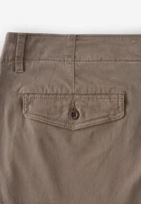 Tan cotton pants with a rear patch pocket, featuring a button closure and a subtle texture. Seam detailing is visible on the fabric.