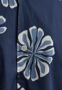 Tengerész stílusú gombos ing, nagy feh�ér és világoskék virágmintákkal, sima anyagból készült, amelynek finom fényessége van.