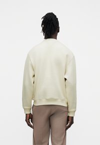 Ανοιχτό μπεζ φούτερ από απαλό ύφασμα, με άνετη γραμμή, στρογγυλή λαιμόκοψη και ριμπ τελειώματα στα μανίκια. Συνδυασμένο με μπεζ παντελόνι.