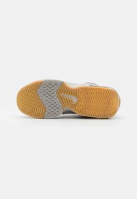 Semelle de chaussure avec un design texturé en gris et orange. Comprend des rainures en zigzag et un logo central, offrant adhérence et traction.