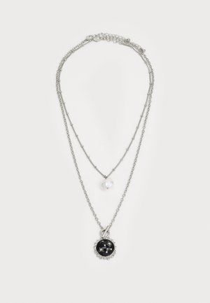 Zilverkleurige gelaagde ketting met een grote zwarte hanger met zilveren accenten en een kleine witte parel op een delicaate ketting.