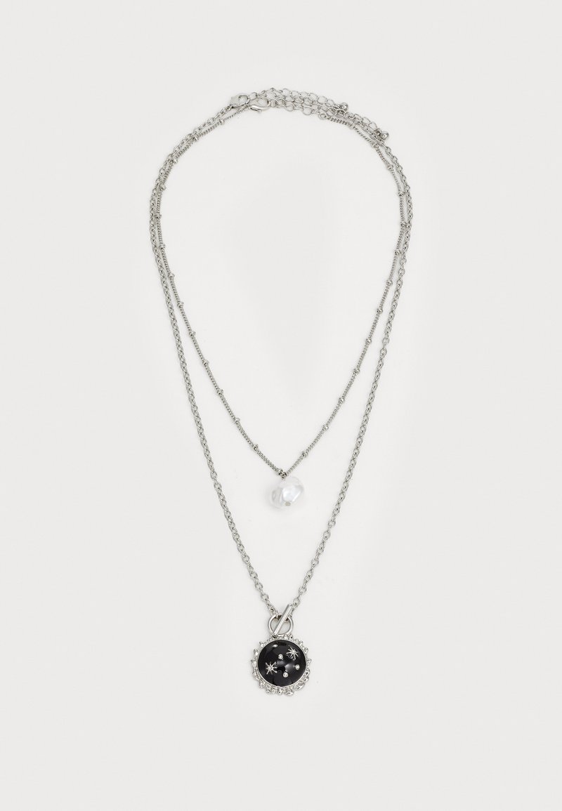 Collier à plusieurs couches en ton argenté, mettant en avant un grand pendentif noir avec des accents argentés et une petite perle blanche sur une chaîne délicate.