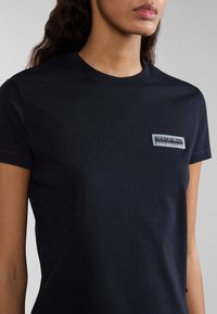 Laivastonsininen t-paita, joka on valmistettu puuvillasta ja jossa on lyhyet hihat. Vasemmassa rintakappaleessa on suorakaiteen muotoinen logopatch. Sileä pinta.