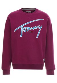 Kaštanová mikina s žebrovanými manžetami a lemem. Má velké bílé logo „Tommy“ a detail červeno-bílo-modré vlajky na hrudi. Hladká textura.