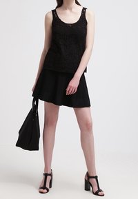 Top de tirantes de encaje negro con cuello redondo, combinado con una falda plisada negra. Incluye un bolso tote negro y sandalias de tacón alto negras con tiras.