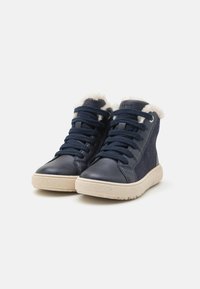 Zapatillas altas de marina con cuero texturizado, forro de piel de peluche y suela de goma. Presentan cordones oscuros y una marca sutil en la lengüeta.
