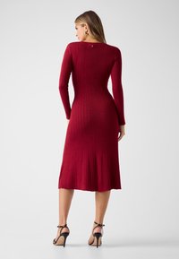 Langärmeliges, geripptes Strickkleid in Burgunderrot, knielang mit ausgestelltem Saum, mit rundem Ausschnitt und Knopfleiste am Rücken.