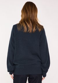 Maglione oversize blu scuro con orlo e polsini a coste, caratterizzato da una texture liscia e un design con spalle scese, visto da dietro.