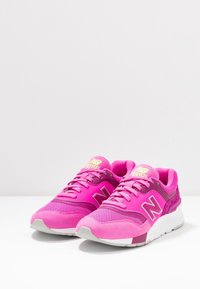 Chaussures de sport roses en mesh et daim, avec un col rembourré, des lacets et une semelle extérieure grise ornée du logo New Balance.