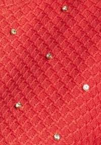Roter strukturierter Stoff mit einem Rautenmuster, verziert mit metallischen Nieten und verstreuten Strassteinen für zusätzliche Details.