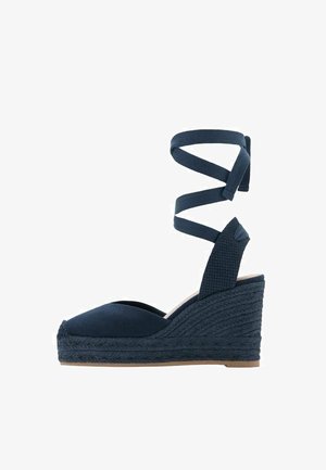 Granatowy sandał na klinie z zakrytymi palcami, plecioną podeszwą na platformie i długimi paskami owiniętymi wokół kostki.