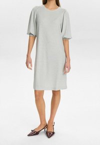 Femme portant une robe gris clair mi-longue avec des manches bouffantes longueur coude et des escarpins slingback pointus bordeaux foncé.