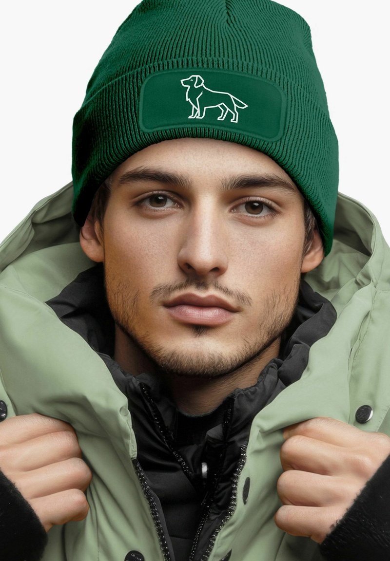 Green knit beanie with a textured pattern and a dog silhouette patch. Worn with a light green puffer jacket over a black inner layer.