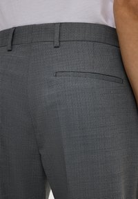 Graue Textilhose mit feinem Karomuster, schlanker Passform und einer einzelnen Gesäßtasche mit minimalistischem schwarzen Paspeldetail.