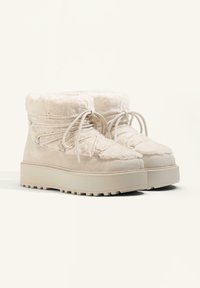 Cream-colored ankle boots with plush fabric upper, textured lace closure, and thick rubber sole, featuring a flat platform design.