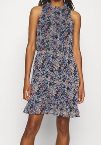 Vestido de estampado floral con un fondo azul marino que presenta flores en tonos rosa, blanco y azul. Diseño sin mangas, con dobladillo con volantes y cinturilla elástica.