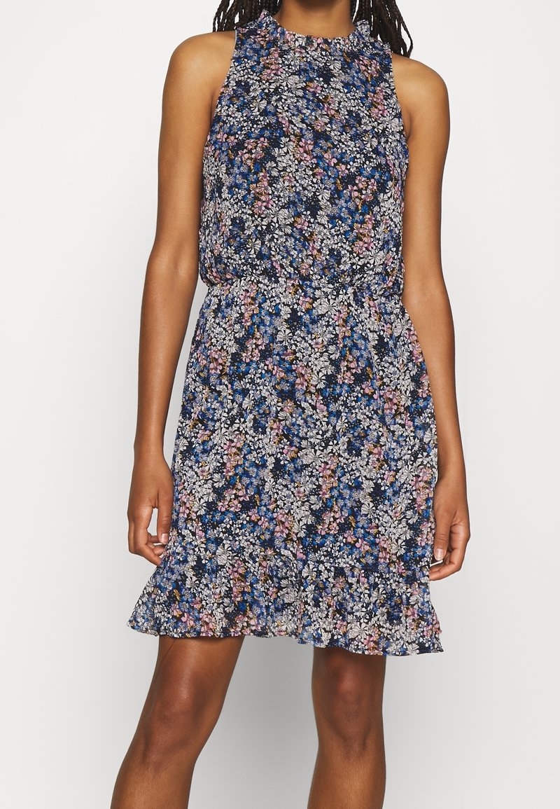 Vestido de estampado floral con un fondo azul marino que presenta flores en tonos rosa, blanco y azul. Diseño sin mangas, con dobladillo con volantes y cinturilla elástica.