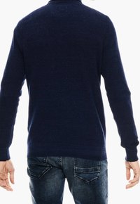 Marinblå ribbad tröja med långa ärmar och rundad halsringning, i kombination med mörkblå denimjeans som har fickdetaljer.