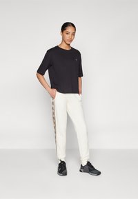 Top corto nero a maniche corte con un piccolo logo sul petto, abbinato a pantaloni jogger bianchi con una striscia laterale fantasia e scarpe da ginnastica nere.