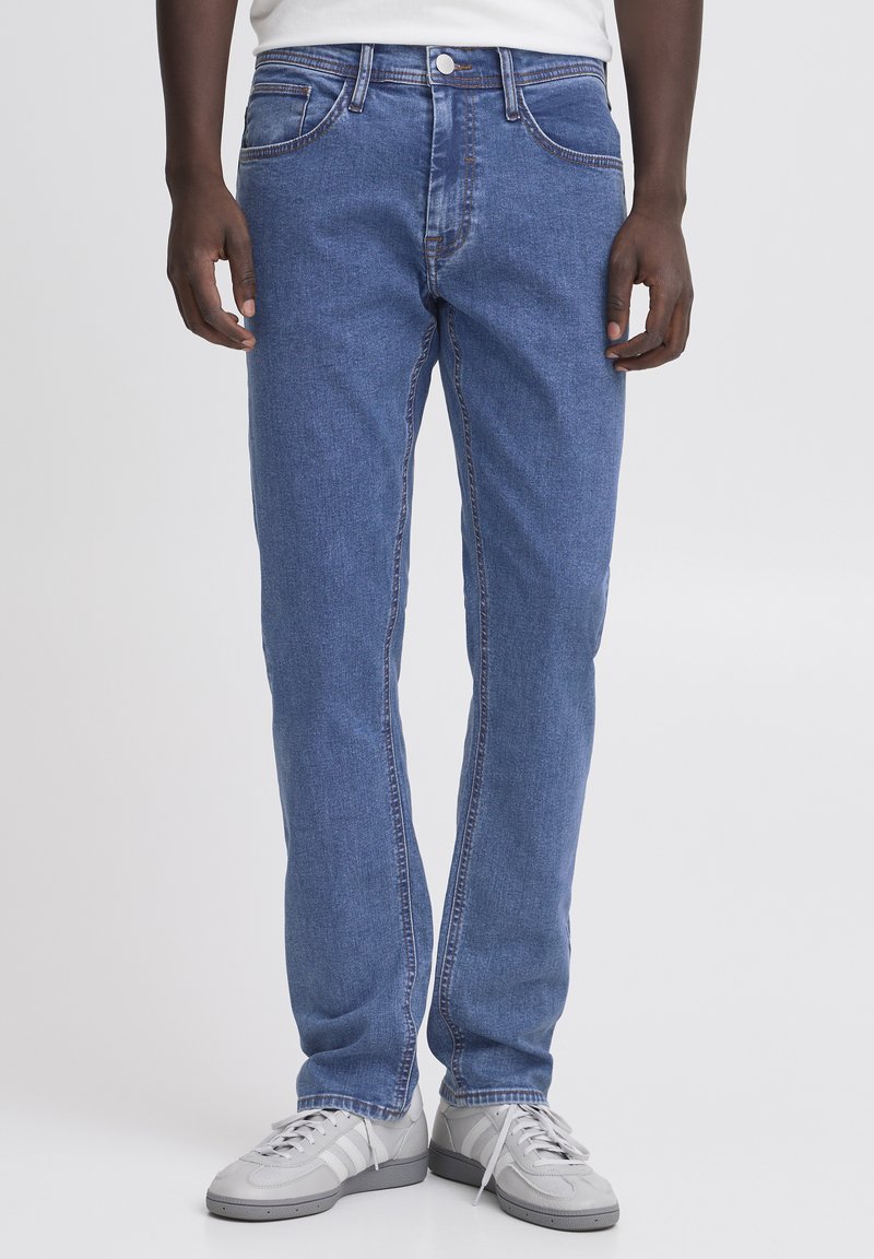 Jeans in denim blu con gamba dritta, cinque tasche e chiusura a bottone argentato; presenta sbiadimenti leggeri e cuciture a contrasto.
