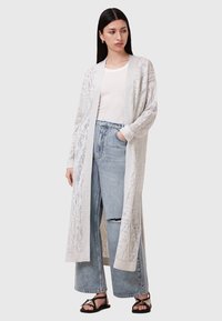 Cardigan leggero e aperto in crema con una texture a motivo, abbinato a jeans in denim blu a vita alta e strappati, e sandali neri.