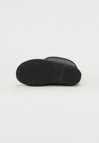 Semelle de botte en caoutchouc noir avec motif de semelle texturé, forme courbée et étiquette de marque. Dessus lisse avec un design de bout arrondi.
