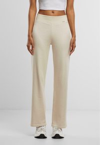 Pantaloni lounge beige a coste con vita alta, caratterizzati da una texture liscia e una vestibilità comoda, abbinati a scarpe da ginnastica bianche.