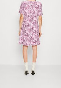 Kortärmad rosa klänning med abstrakta vita och mörkrosa mönster, semi-utställd kjolstil, kombinerad med knähöga off-white klackstövlar.