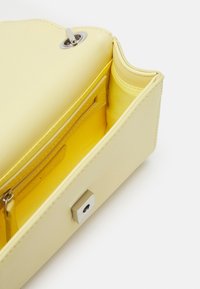 Inredning av gul läderhandväska med slät textur, ficka med dragkedja och silverfärgade beslag. Har en mjuk, rundad design.