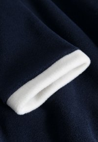 Marineblaue Fleece-Stoff mit einer weichen weißen Einfassung am Rand, der eine glatte Textur und ein gefaltetes Manschettendesign zeigt.