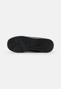 Sole di scarpa da ginnastica nera in gomma con motivi di battistrada testurizzati, caratterizzata da scanalature angolari e un logo discreto. Finitura liscia, design durevole.