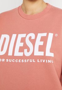Kapuzenpullover aus Baumwolle in Pfirsich mit weißem Text "DIESEL" und "FÜR EIN ERFOLGREICHES LEBEN." Gerippter Ausschnitt und weiche Textur.