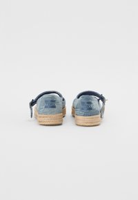 Espadrilhas de denim com parte superior de tecido azul, sola de corda de juta e uma alça traseira para suporte. Textura suave e design simples.