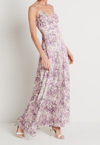 Robe longue fleurie aux teintes lavande et vertes, réalisée en tissu léger. Elle présente des bretelles fines et une silhouette fluide avec un décolleté en V.