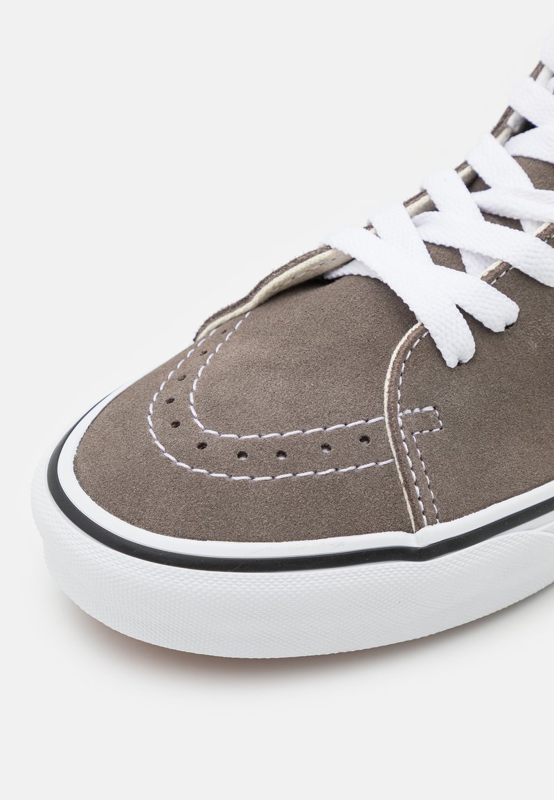 Zapatilla de ante gris con cordones blancos, costuras blancas en contraste y suela de goma negra. Punta redondeada y detalles perforados en la parte superior.