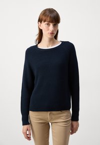 Suéter em malha canelada de cor navy com gola redonda e mangas longas. Apresenta um padrão texturizado e punhos ajustados, combinado com calças bege.