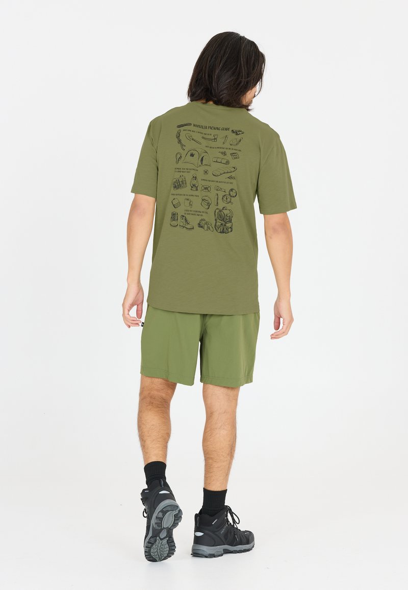 Homme portant un t-shirt vert olive avec des illustrations d'équipement de camping au dos, un short assorti, des chaussettes noires et des chaussures de randonnée noires, marchant de dos.