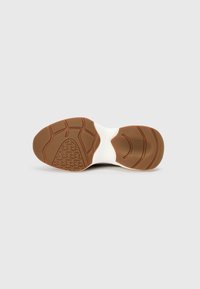 Shoe sole with a brown rubber bottom featuring a textured grip pattern. White midsole, slightly curved shape, smooth surface.