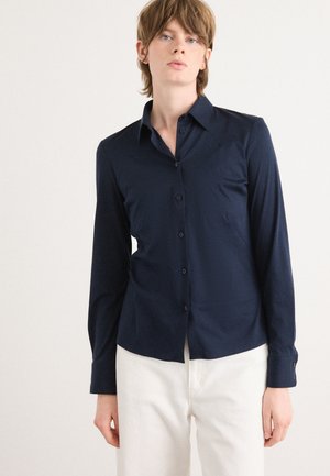 Camicia a maniche lunghe blu navy con colletto button-down, caratterizzata da una vestibilità su misura, una texture liscia e un leggero stretch. Bottoni allineati sul davanti.