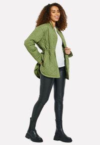 Giacca imbottita verde oliva con vita elastica, bottoni a pressione e due tasche. Abbinata a leggings in pelle nera e stivaletti neri chunky.
