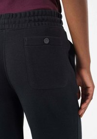 Zwarte joggingbroek met een geribbelde tailleband, voorzien van een achterzak met knoopsluiting en een gladde katoenstructuur.