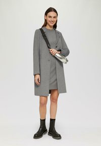 Manteau en laine grise avec revers notch, superposé à une robe assortie. Bottes à plateformes noires transparentes. Sac argenté avec une bandoulière.
