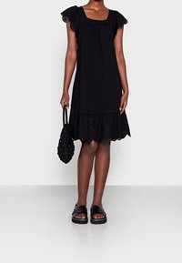 Vestito nero con orlo rifinito in pizzo, design a strati e maniche corte arricciate. Abbinato a una borsa nera testurizzata e sandali.